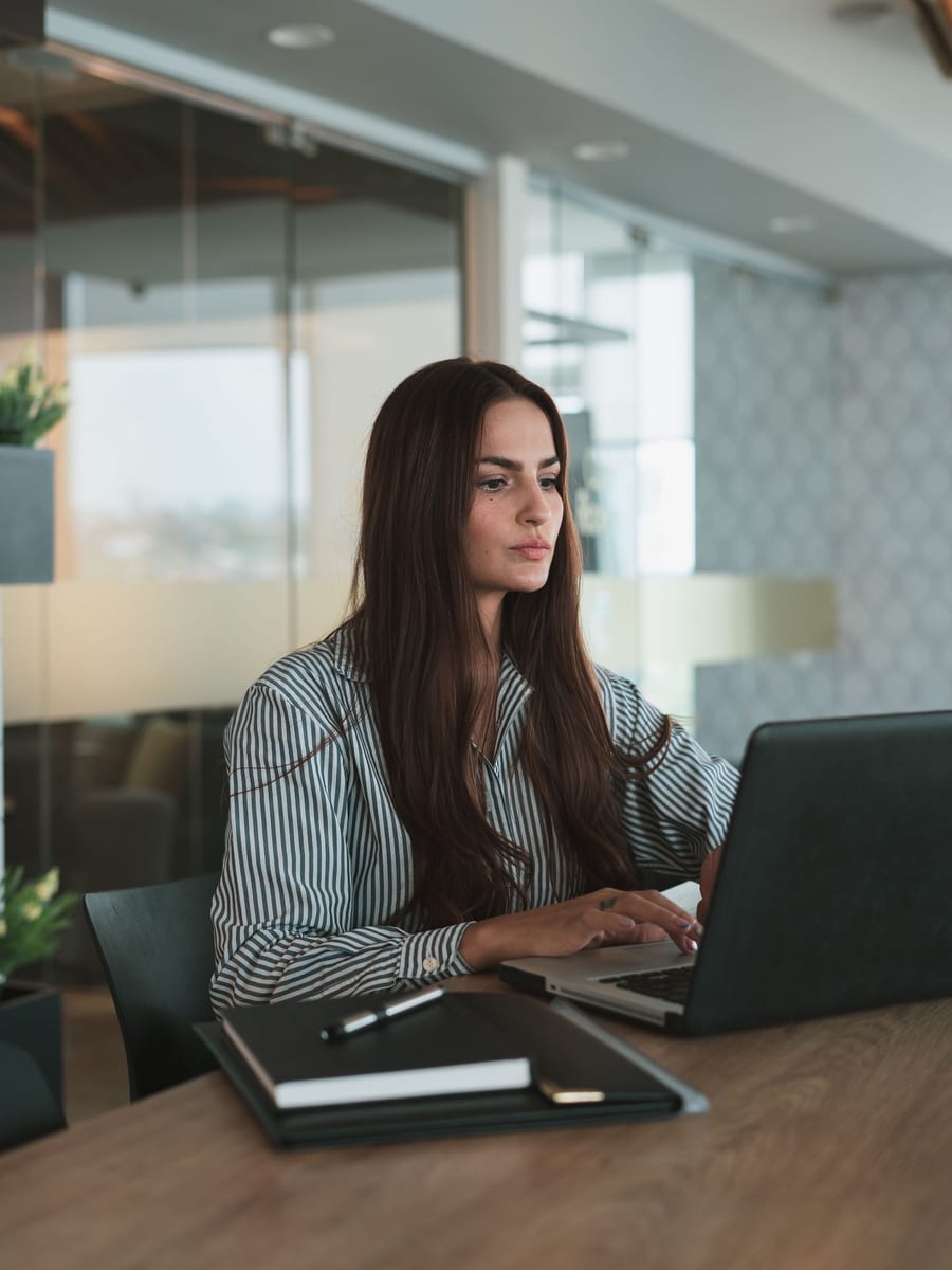 A marketing lead at her laptop in a glass-walled office, working through the week's posts